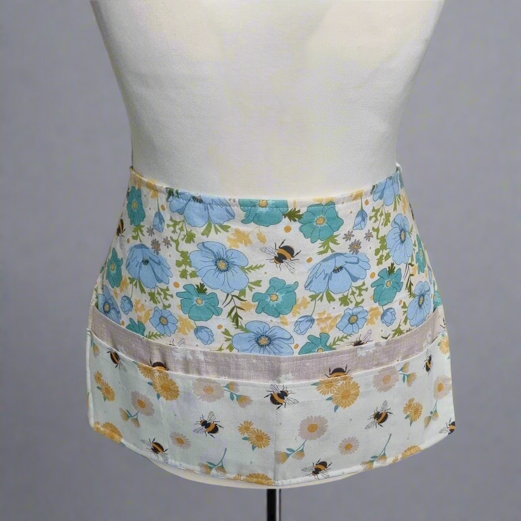 Floral apron with bee design on a mannequin against a gray background