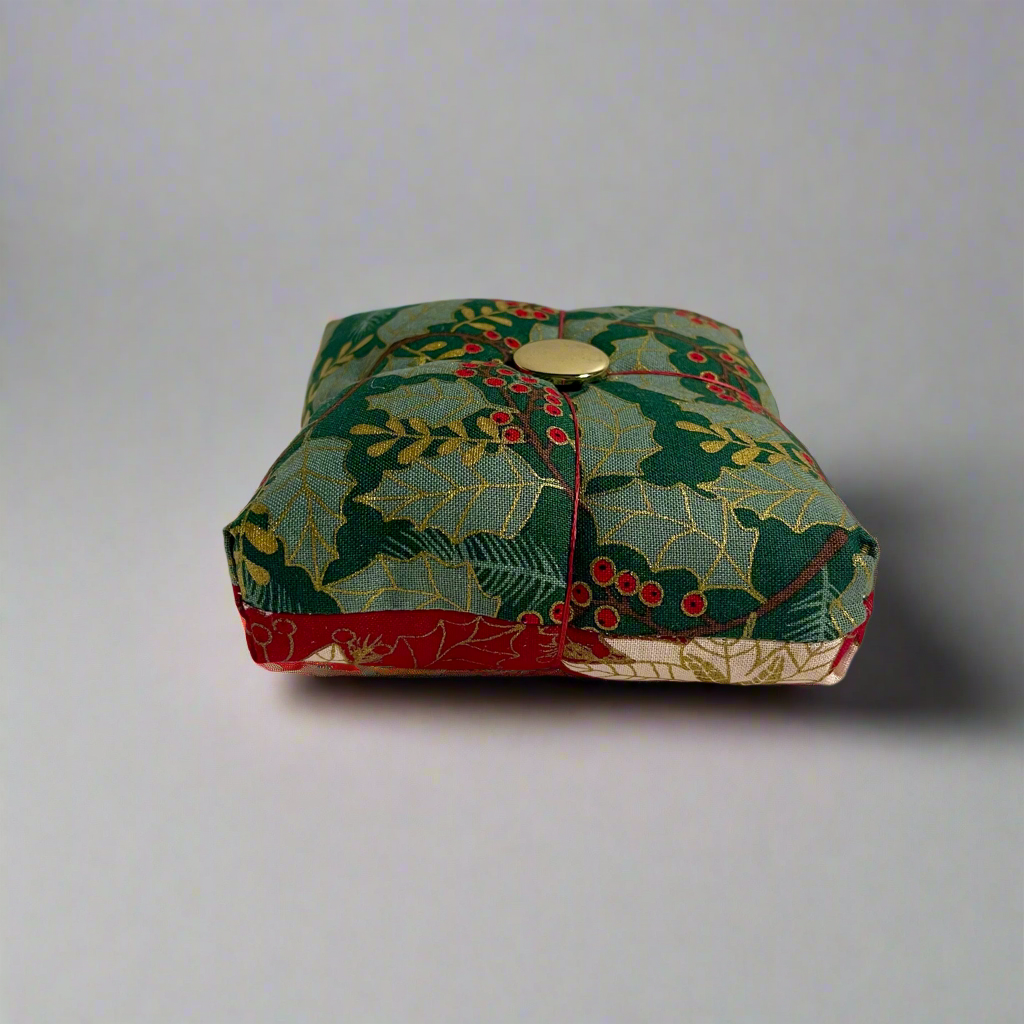 Decorative fabric pincushion with holly design on a plain background