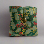 Fabric pincushion with holly leaf pattern and gold button on a gray background