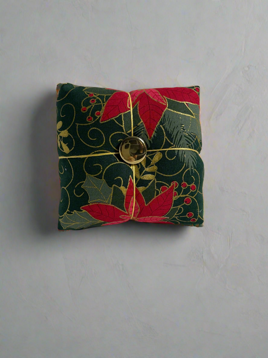 Small green fabric pincushion with red floral patterns on a gray background