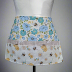 Floral apron with bee pattern on a mannequin against a gray background