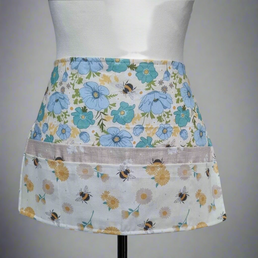 Floral apron with bee pattern on a mannequin against a gray background