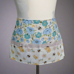 Floral apron with blue flowers and bees on a mannequin against a gray background