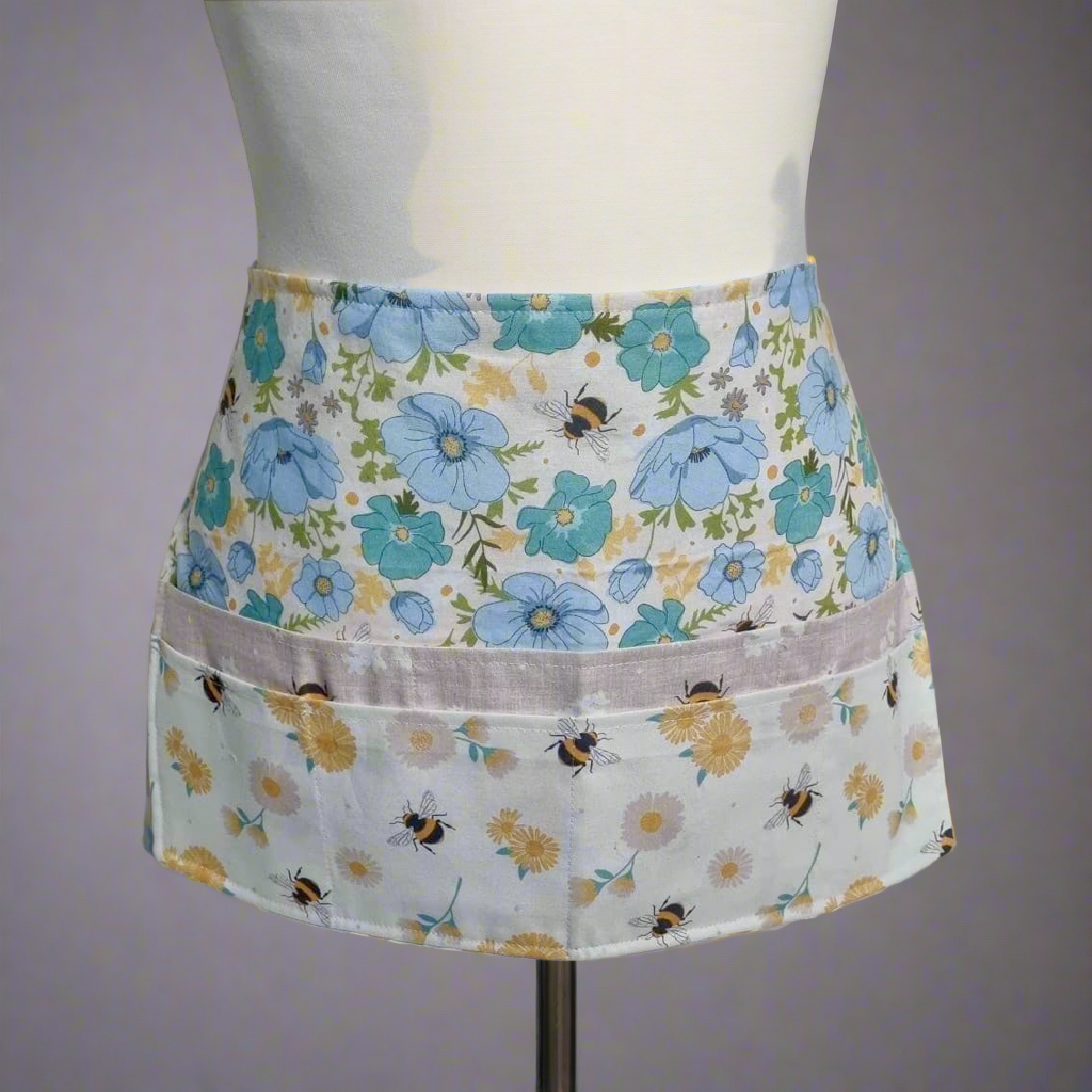 Floral apron with blue flowers and bees on a mannequin against a gray background