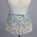 Floral apron with bee design on a mannequin against a gray background