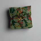 Decorative fabric pincushion with holly design and gold button on a white background