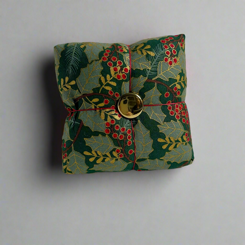 Decorative fabric pincushion with holly design and gold button on a white background