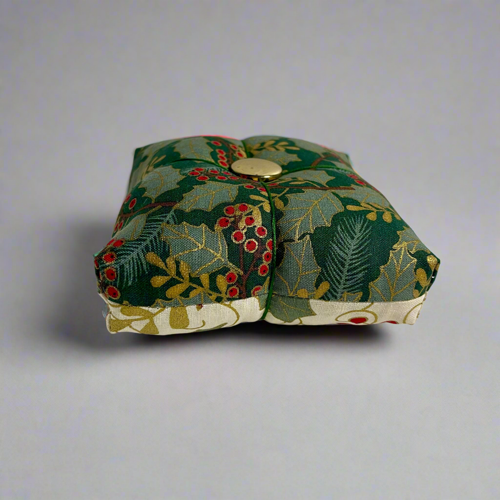 Small fabric pincushion with holly design on a light gray background