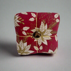 Red fabric pincushion with gold and white leaf pattern and a gold button on a gray background